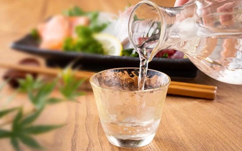 Water being poured into glass with sushi ingredients and chopsticks on wooden table