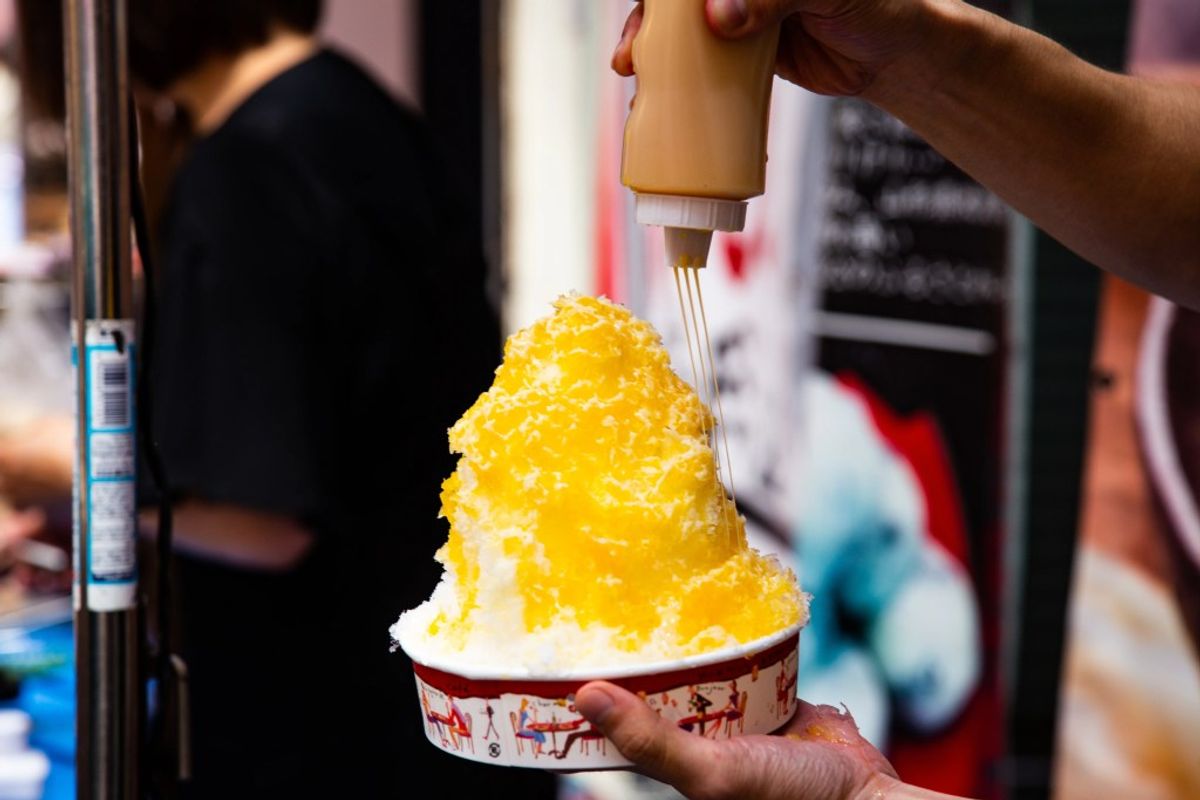 Shaved ice dessert with yellow syrup being drizzled on top at food stall