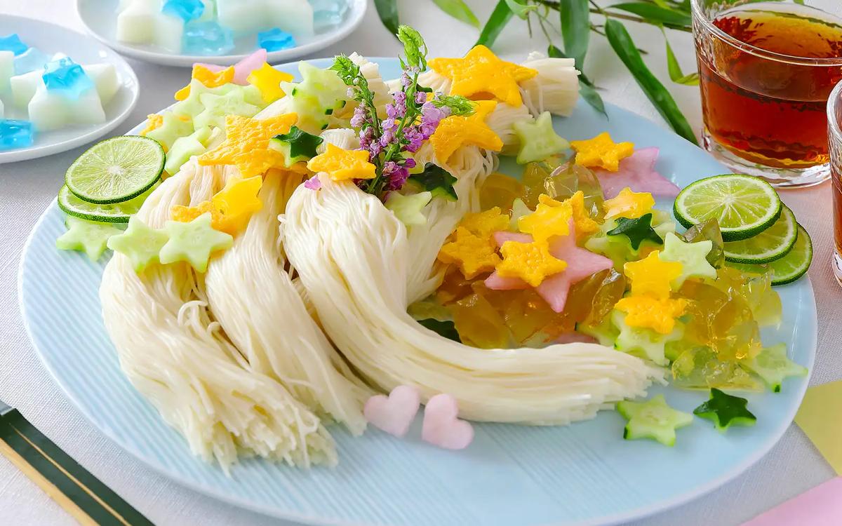 Decorative rice noodles with colorful jelly stars, lime slices, and edible flowers on blue plate