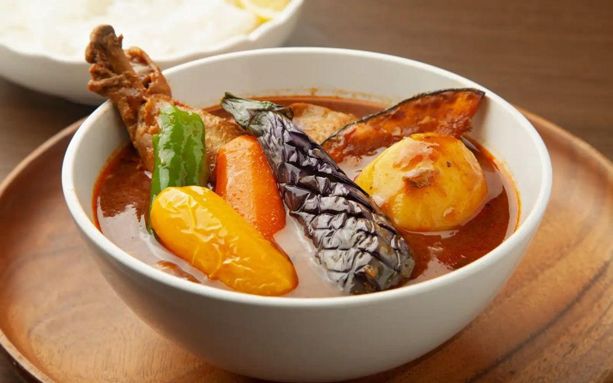 Fish stew with eggplant, potato, red pepper, and herb garnish in broth