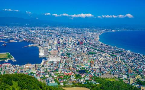 Aerial view of coastal Japanese city with harbor, mountains, and blue sea