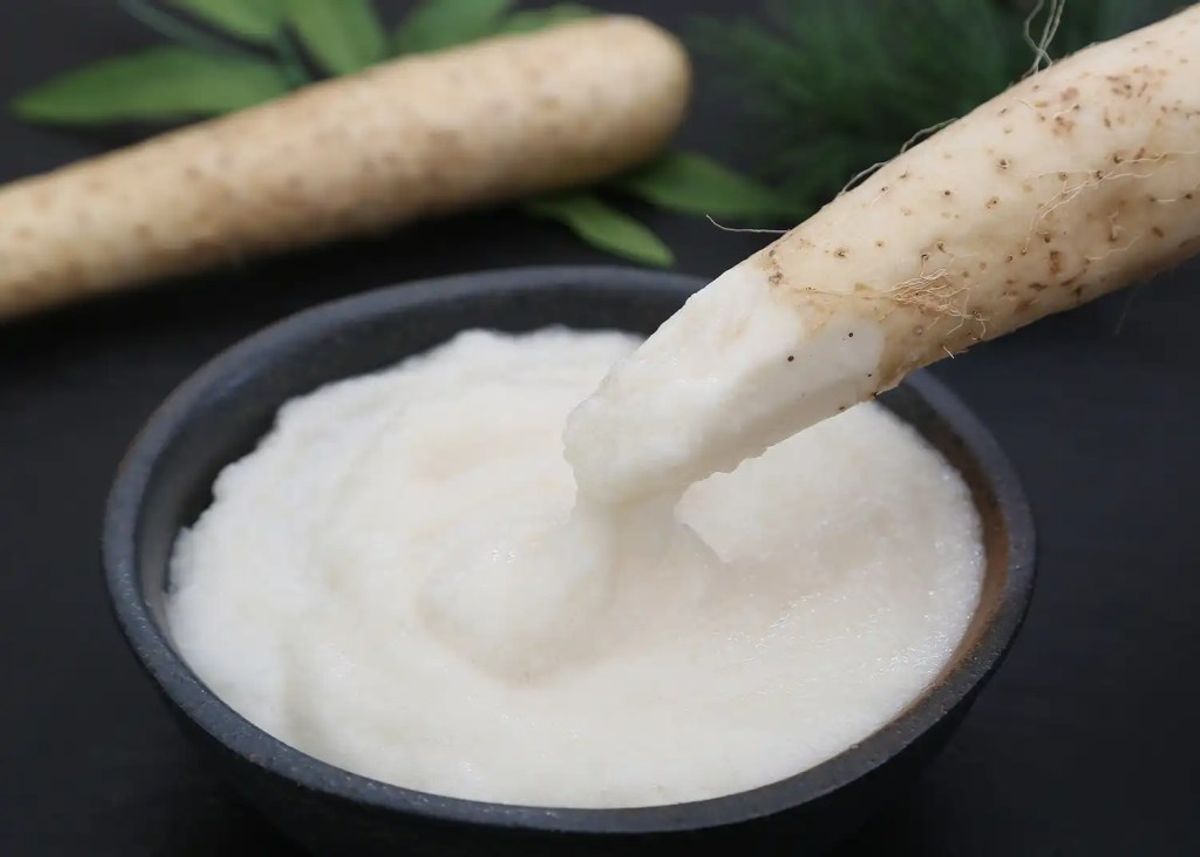 Wasabi root being grated into white paste in ceramic bowl with fresh wasabi in background