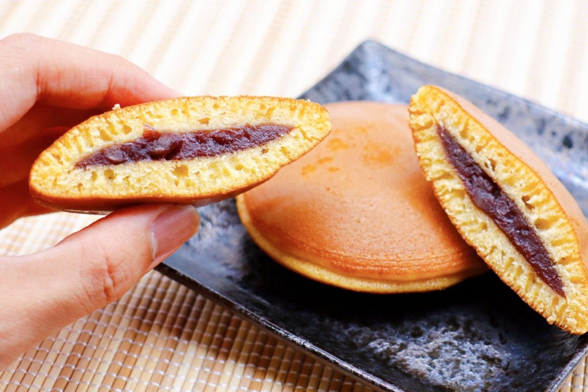 Hand holding dorayaki with red bean filling, two more on black plate