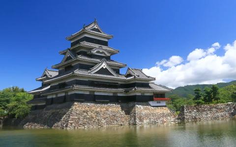 Japanese castle with tiered roofs on stone foundation beside moat and mountains