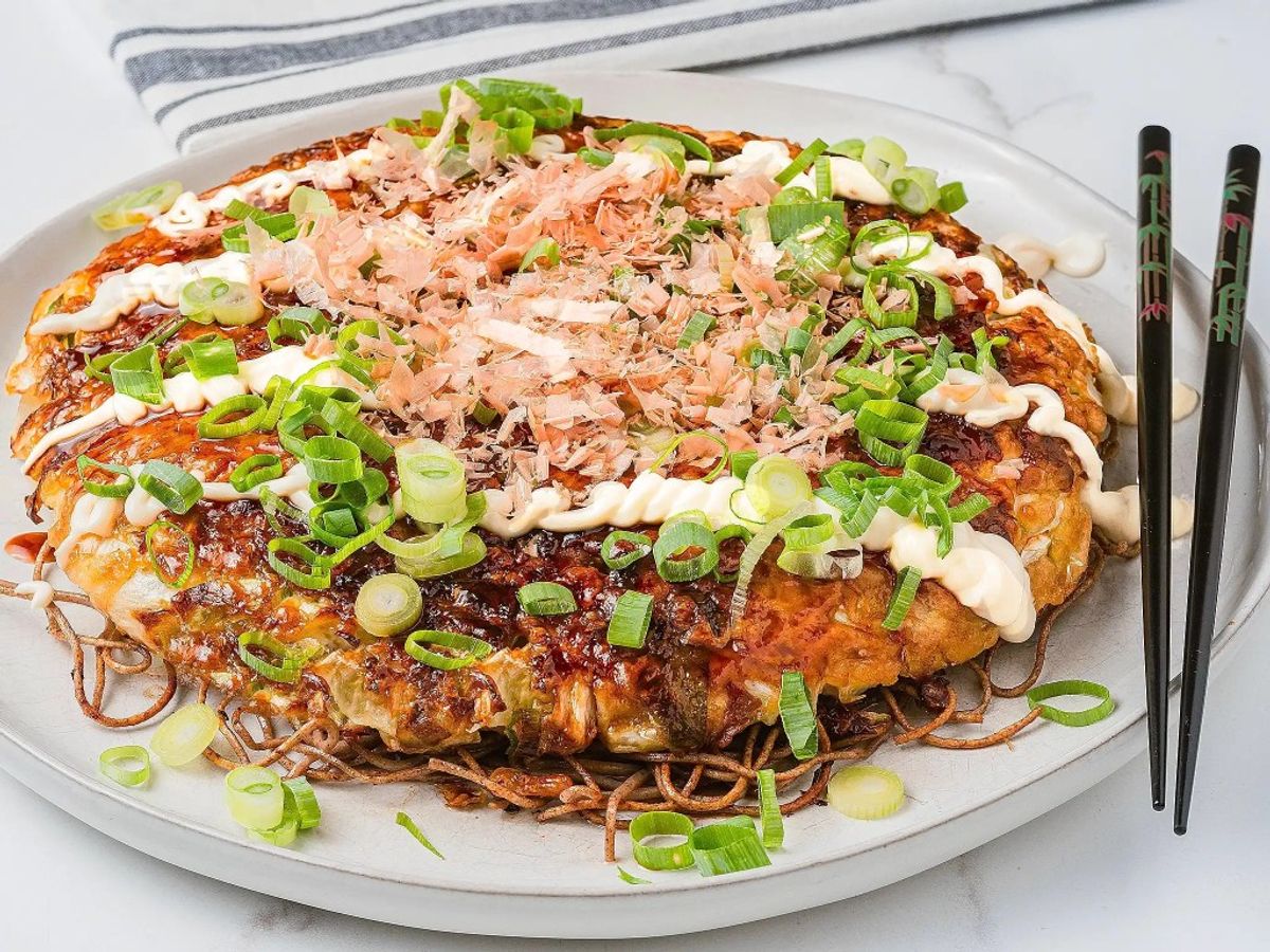 Okonomiyaki topped with bonito flakes, mayonnaise, and green onions on white plate