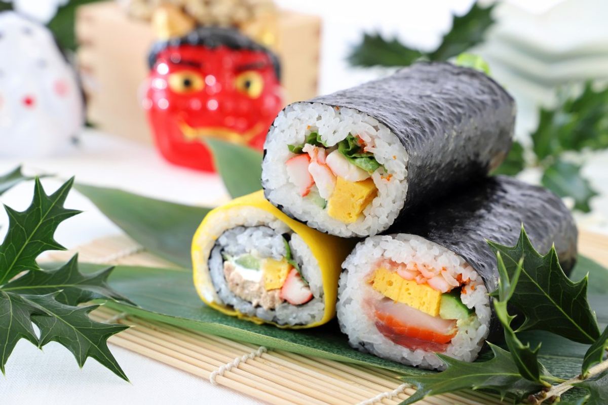 Sushi rolls with nori seaweed, shrimp, and vegetables on bamboo mat with holly decorations
