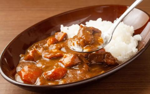 Beef curry over white rice in brown bowl with spoon, wooden table