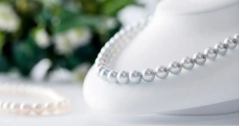 Pearl necklaces displayed on white mannequin busts with flowers in background