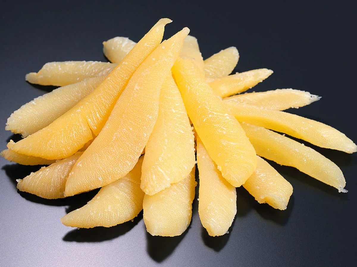 Peeled yuzu citrus fruit segments arranged in a circular pattern on dark surface