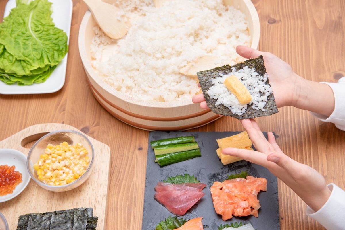 Sushi preparation with nori, rice, seafood, cucumber, and tamago on wooden table