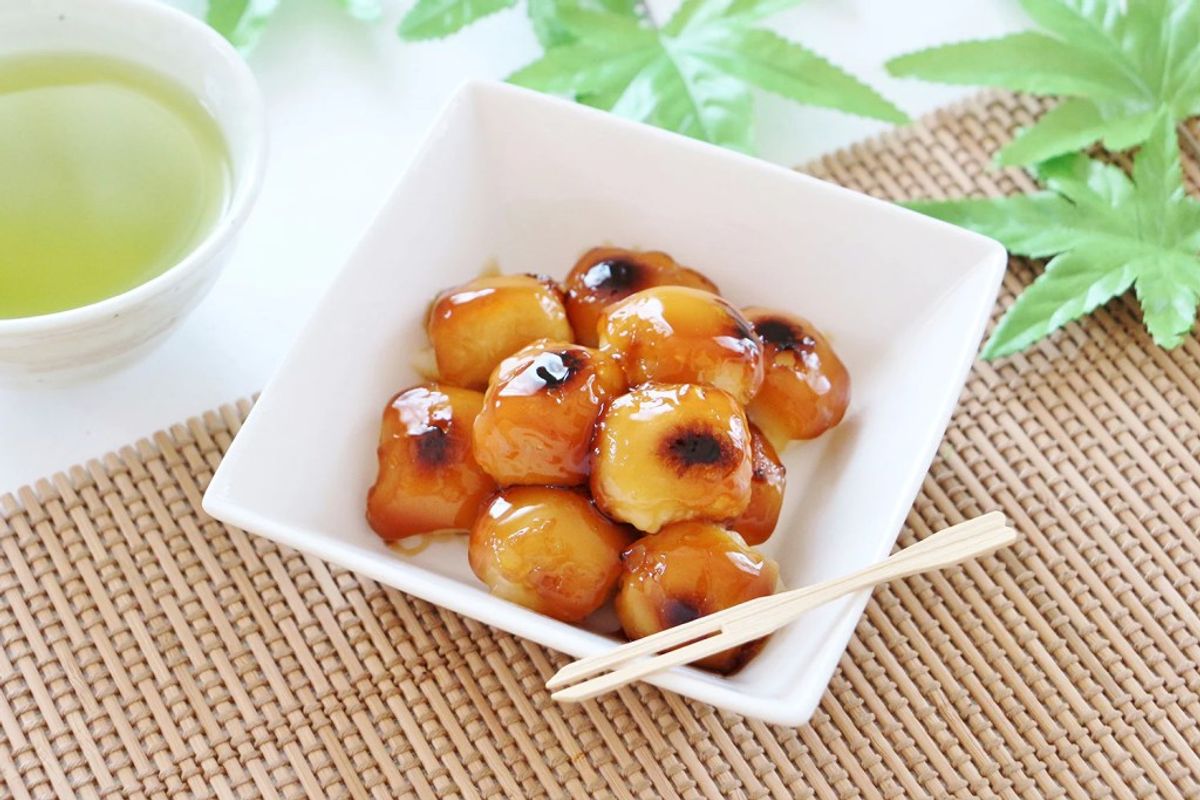 Glazed dango dumplings in white bowl with green tea and chopsticks on woven placemat