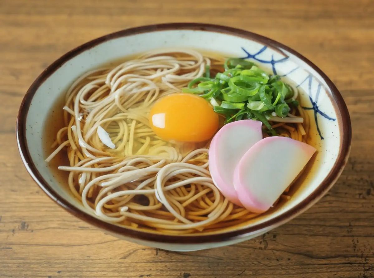 Bowl of ramen with raw egg yolk, pickled ginger, green onions, and broth on wooden table