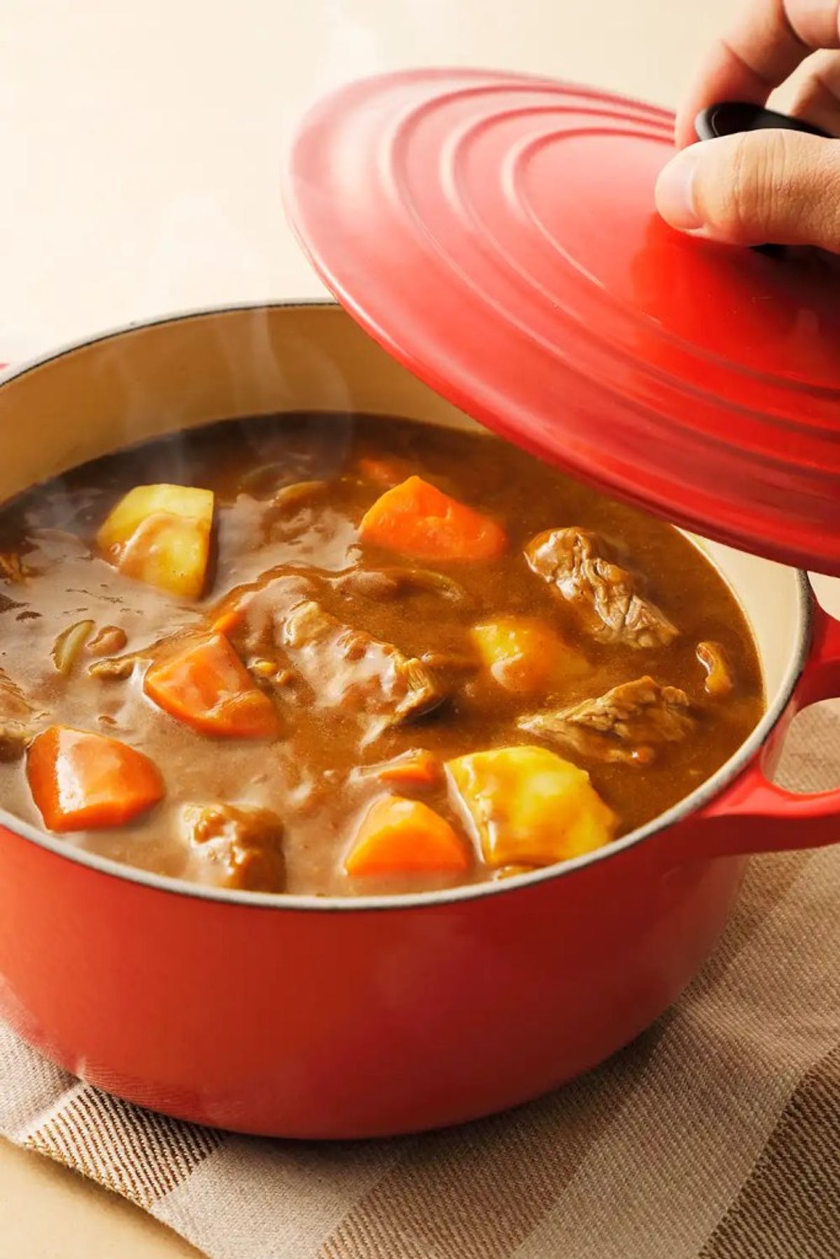 Red Dutch oven with beef stew, potatoes, and carrots being covered with lid