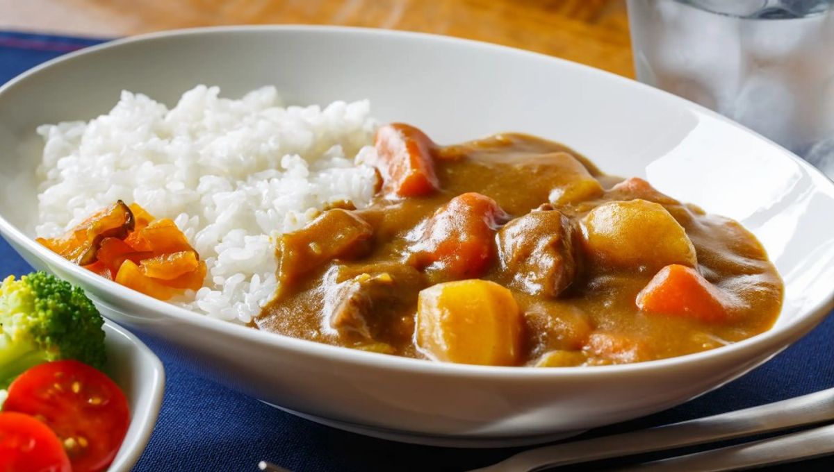 Curry rice with beef, potatoes, and carrots served on white plate with fresh vegetables