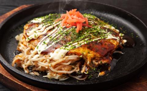 Okonomiyaki served on black cast iron plate with bonito flakes, mayo, pickled ginger