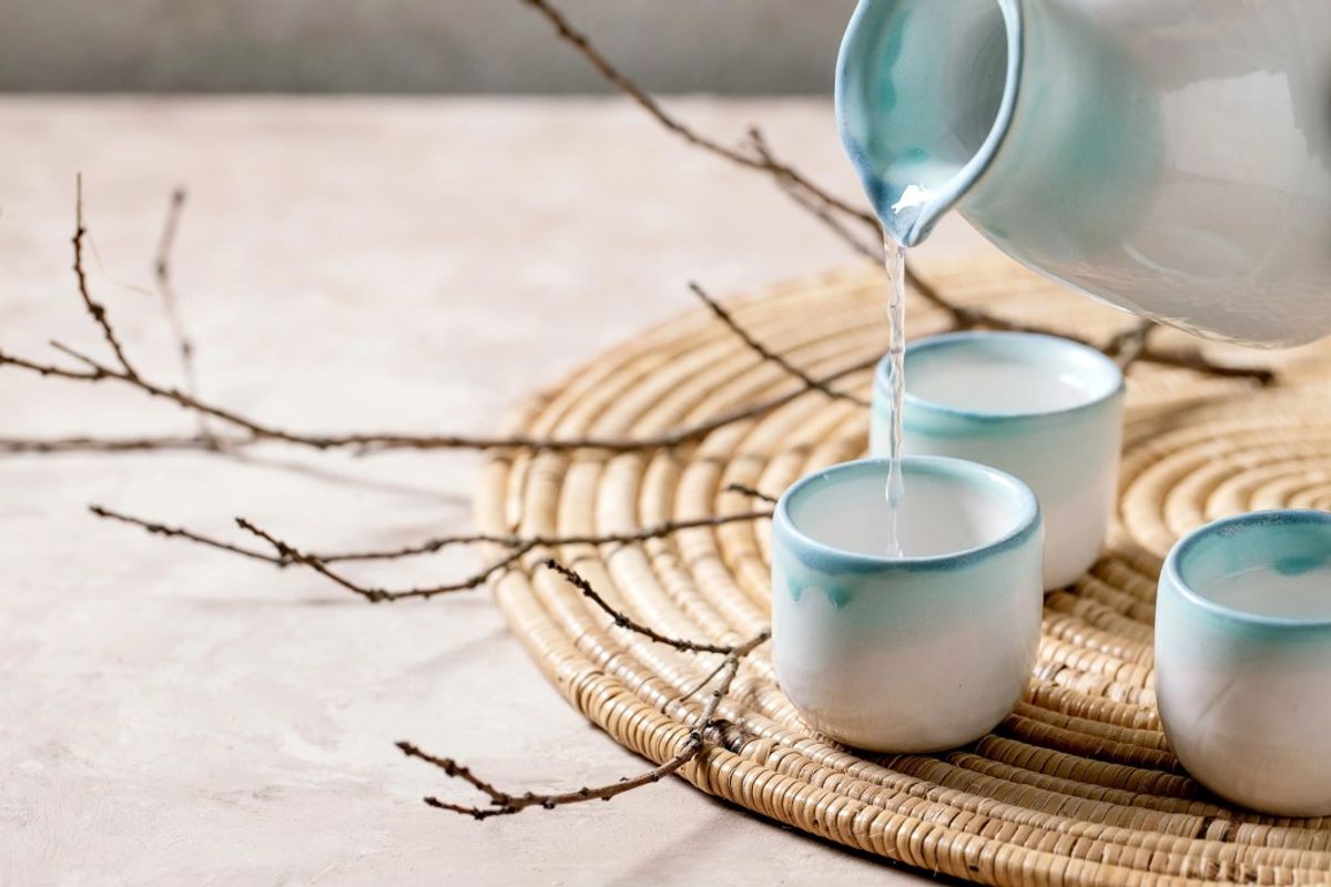 Water pouring into ceramic cups on woven placemat with decorative branches