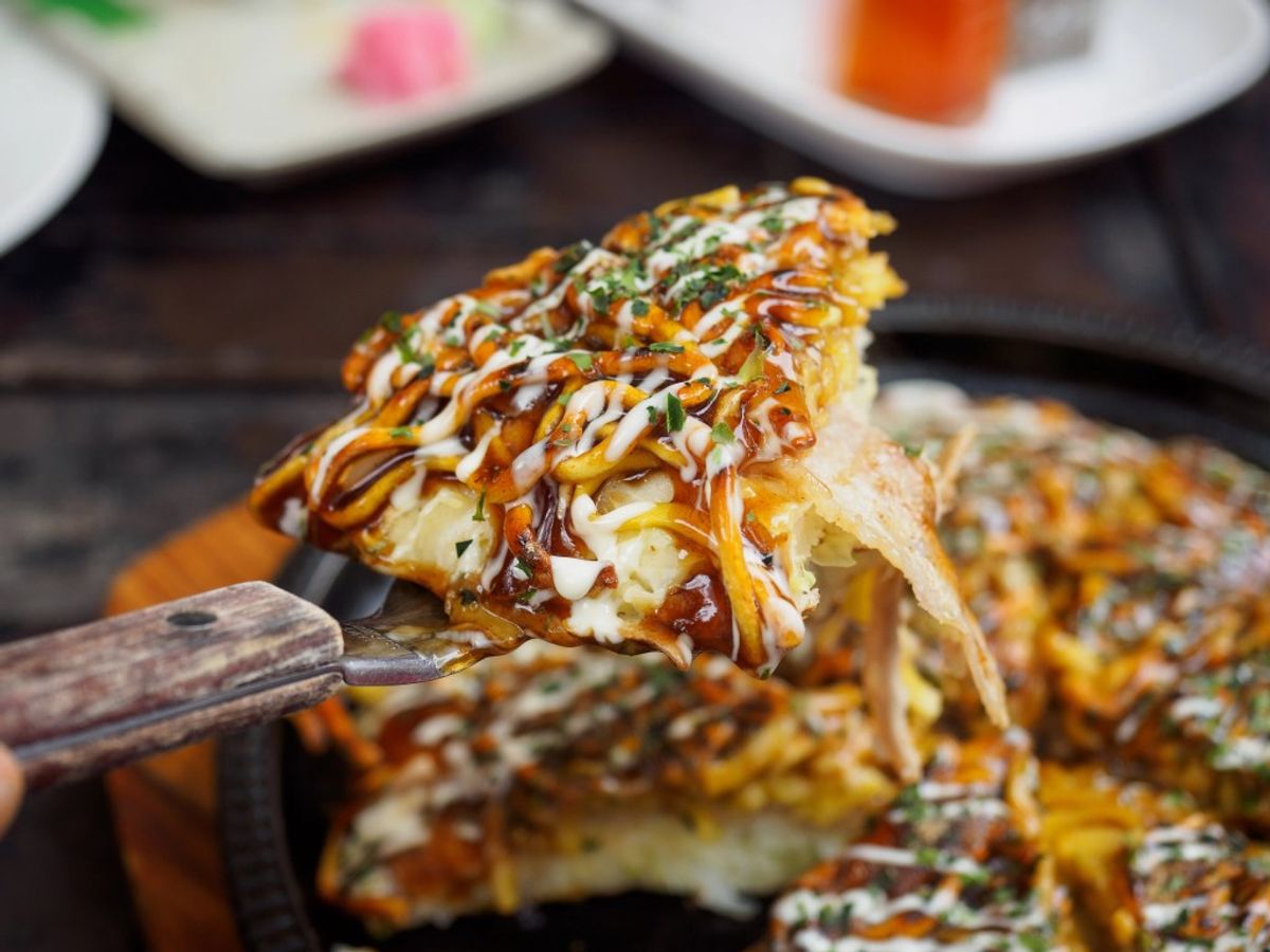 Okonomiyaki topped with bonito flakes, mayo drizzle, and aonori powder on spatula