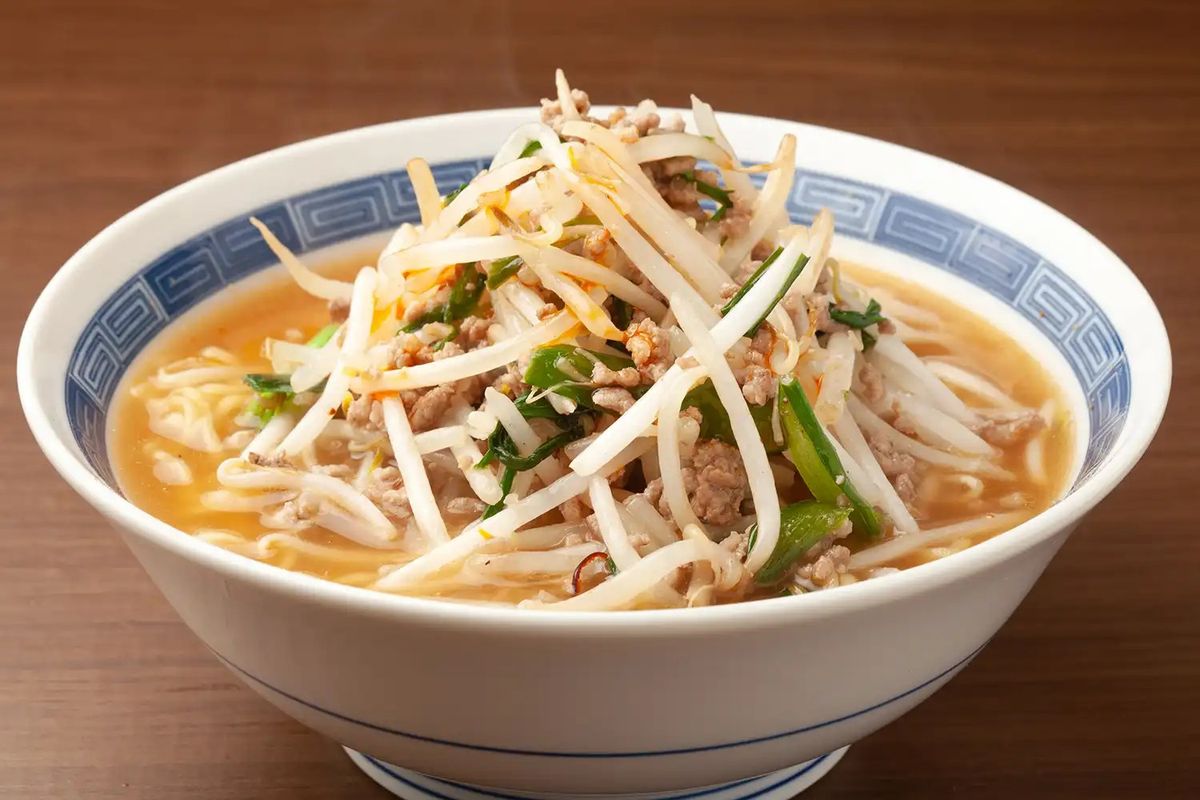 Bowl of ramen with ground meat, bean sprouts, green onions, and broth in white ceramic bowl