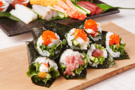 Assorted sushi hand rolls with ikura, tuna, and fresh vegetables on wooden board