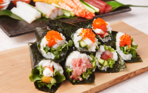 Assorted sushi hand rolls with ikura, tuna, and fresh vegetables on wooden board
