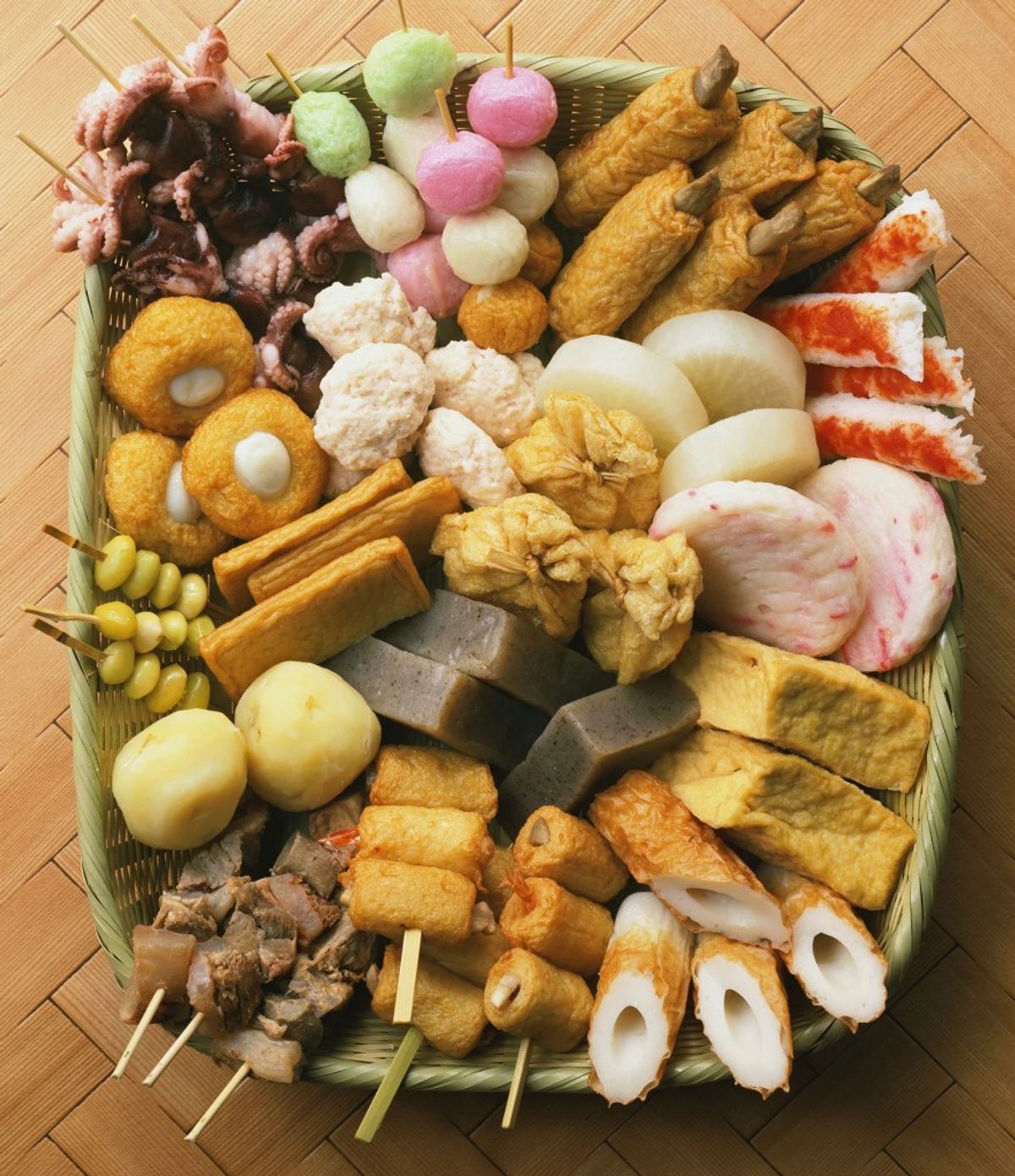 Assorted oden ingredients arranged in woven basket on wooden floor