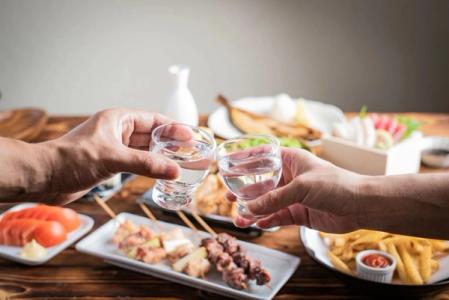 Two people toasting with water glasses at dining table surrounded by various dishes and appetizers