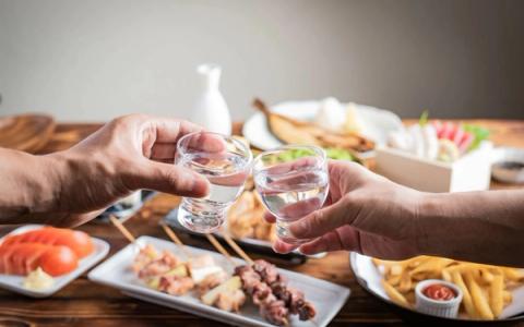 Two people toasting with water glasses at dining table surrounded by various dishes and appetizers