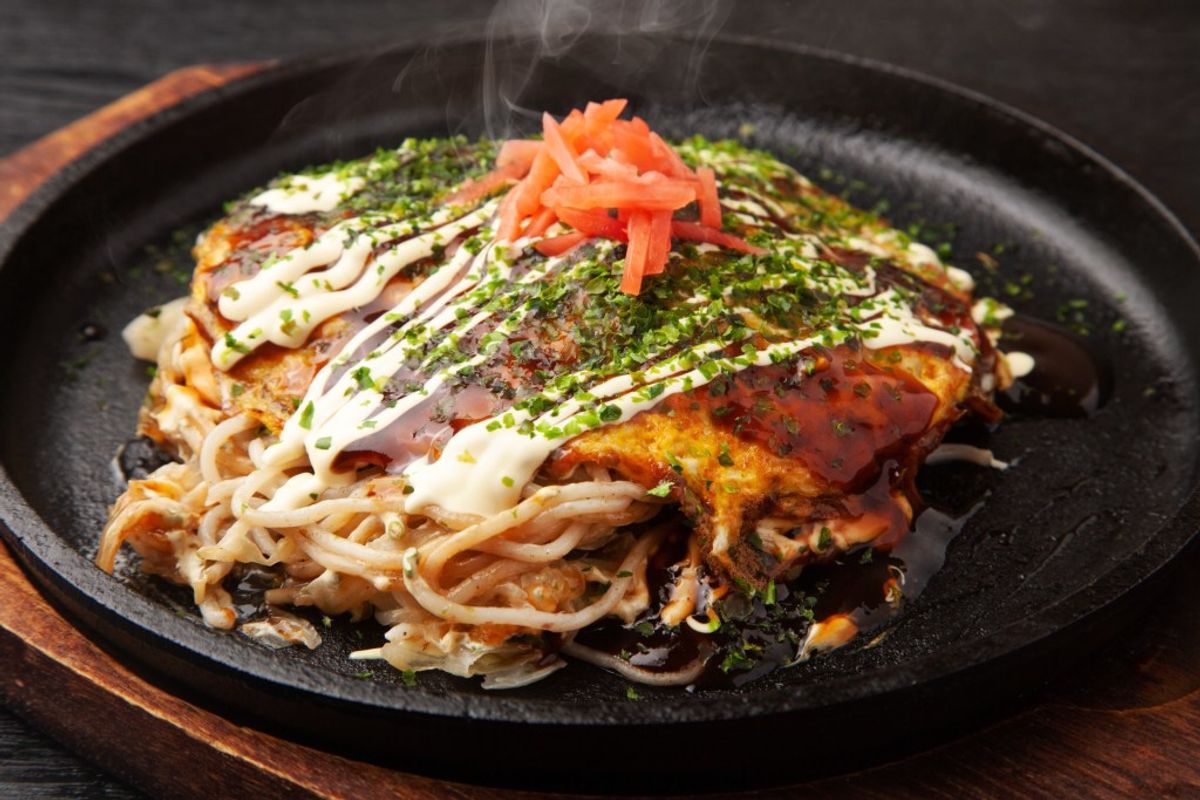 Okonomiyaki served on black plate with bonito flakes, mayo drizzle, pickled ginger