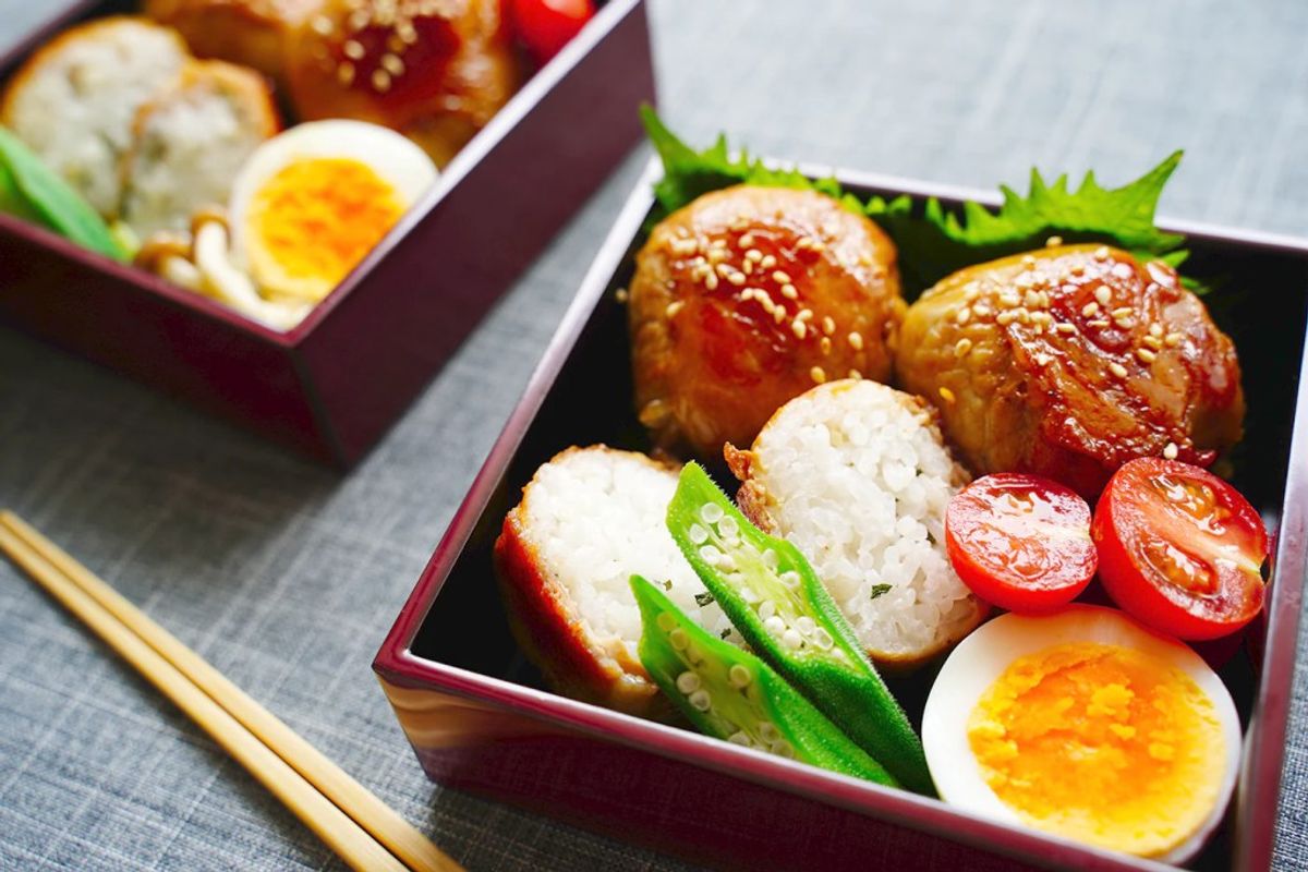 Bento boxes with ramen noodles, soft-boiled eggs, tomatoes, green onions, and chopsticks