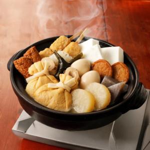 Hot pot with fish cake, tofu, mushrooms, and vegetables in black ceramic bowl