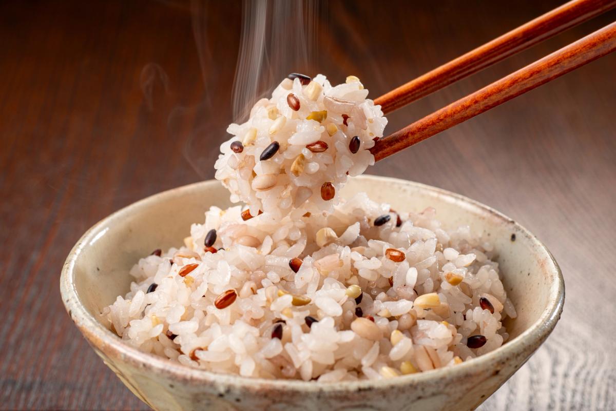 Chopsticks lifting cooked rice with red beans from ceramic bowl