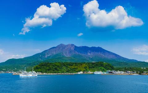 Sakurajima volcano with coastal town and ferry boat under blue sky