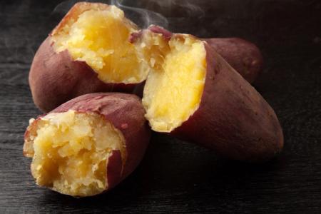 Roasted sweet potatoes with steaming flesh exposed on dark wooden surface