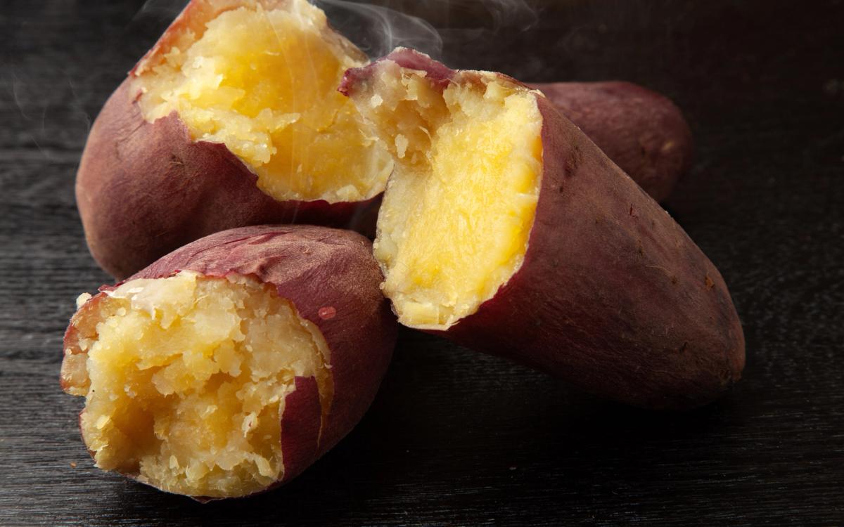 Roasted sweet potatoes with steaming flesh exposed on dark wooden surface