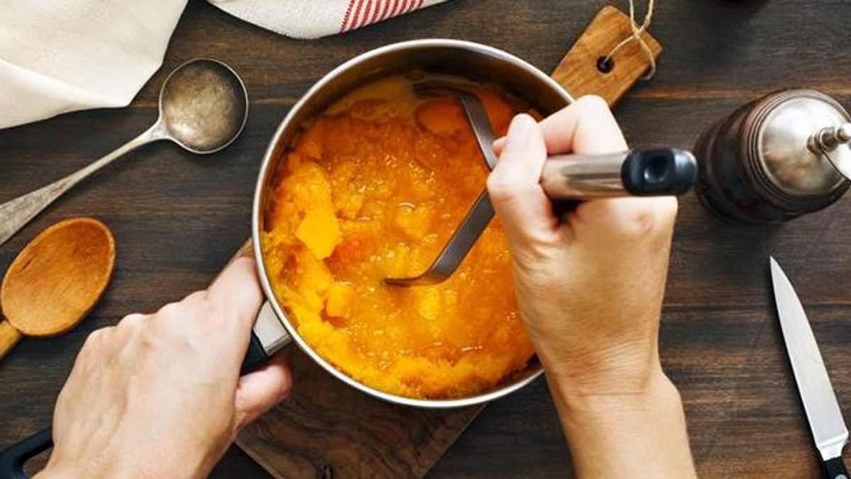 Chef stirring golden soup or broth in pot with wooden spoon, cooking utensils on dark table