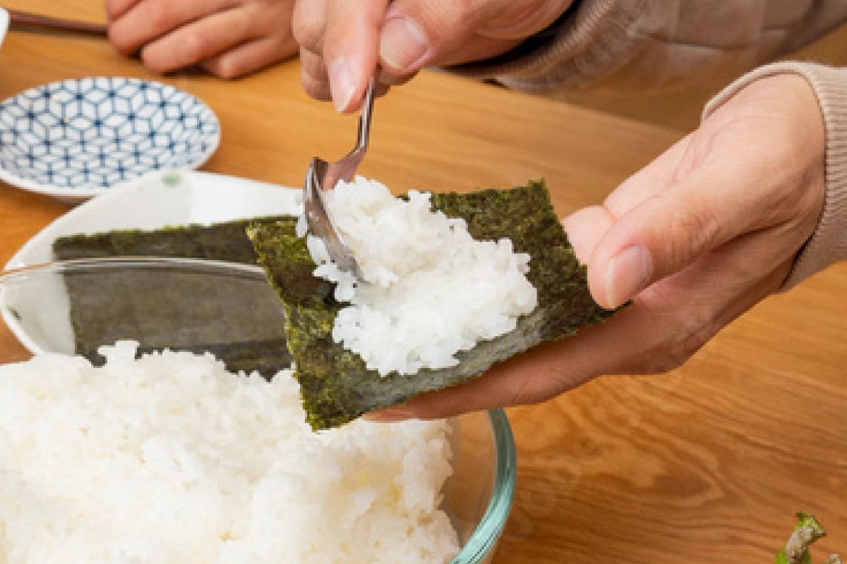 Person spreading rice on nori sheet with fork for sushi preparation