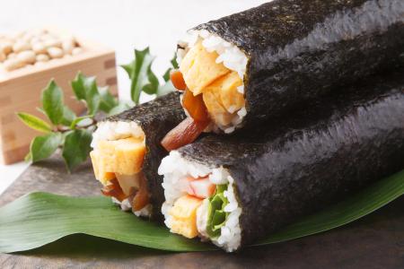 Sushi rolls wrapped in nori seaweed with tamago, imitation crab, and vegetables on green leaf