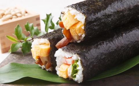 Sushi rolls wrapped in nori seaweed with tamago, imitation crab, and vegetables on green leaf