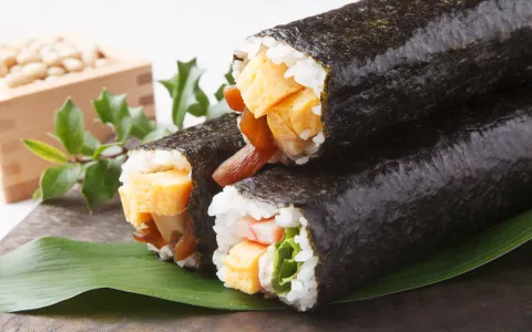 Sushi rolls wrapped in nori seaweed with tamago, imitation crab, and vegetables on green leaf