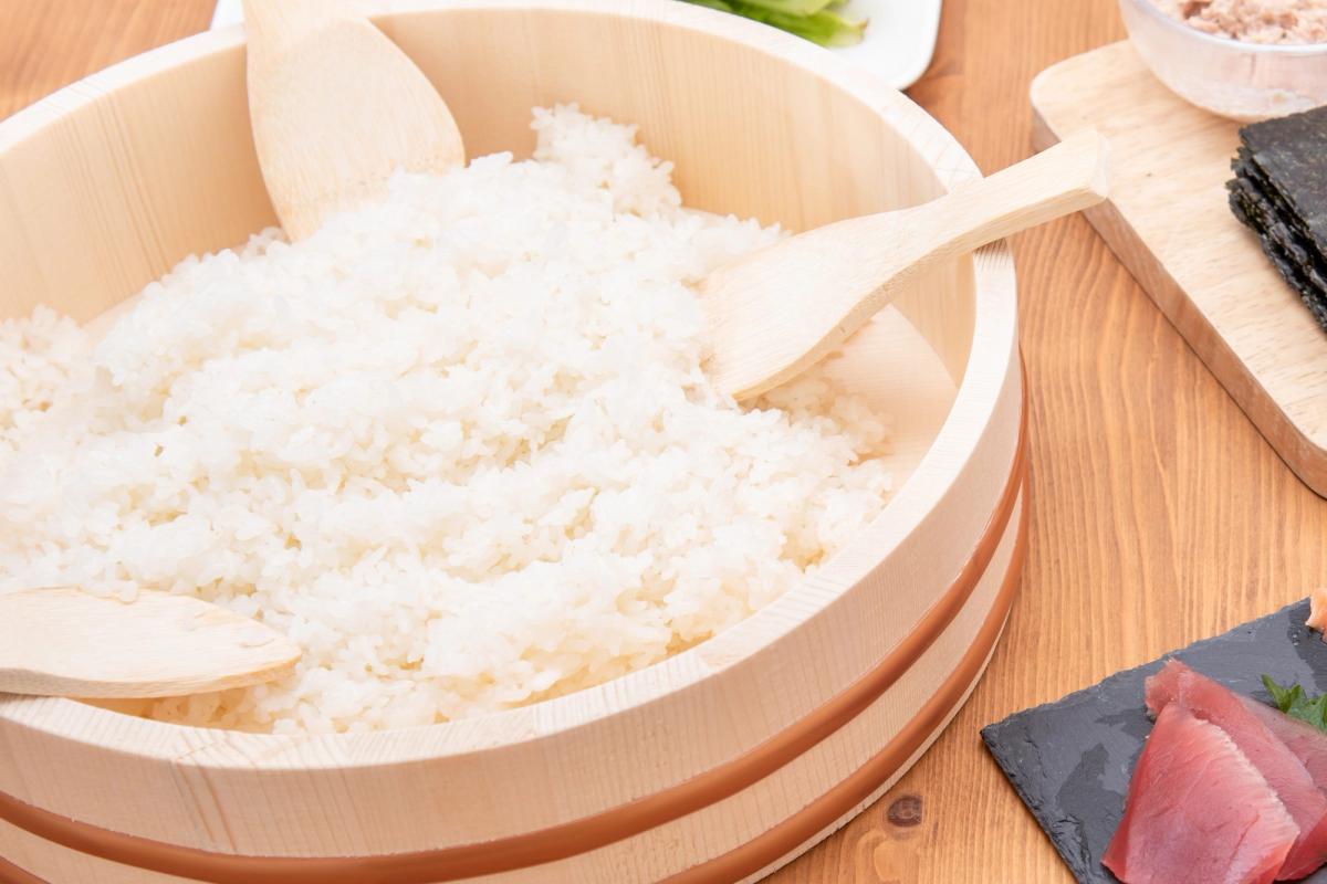 Freshly steamed white rice in wooden bamboo steamer basket with wooden paddle