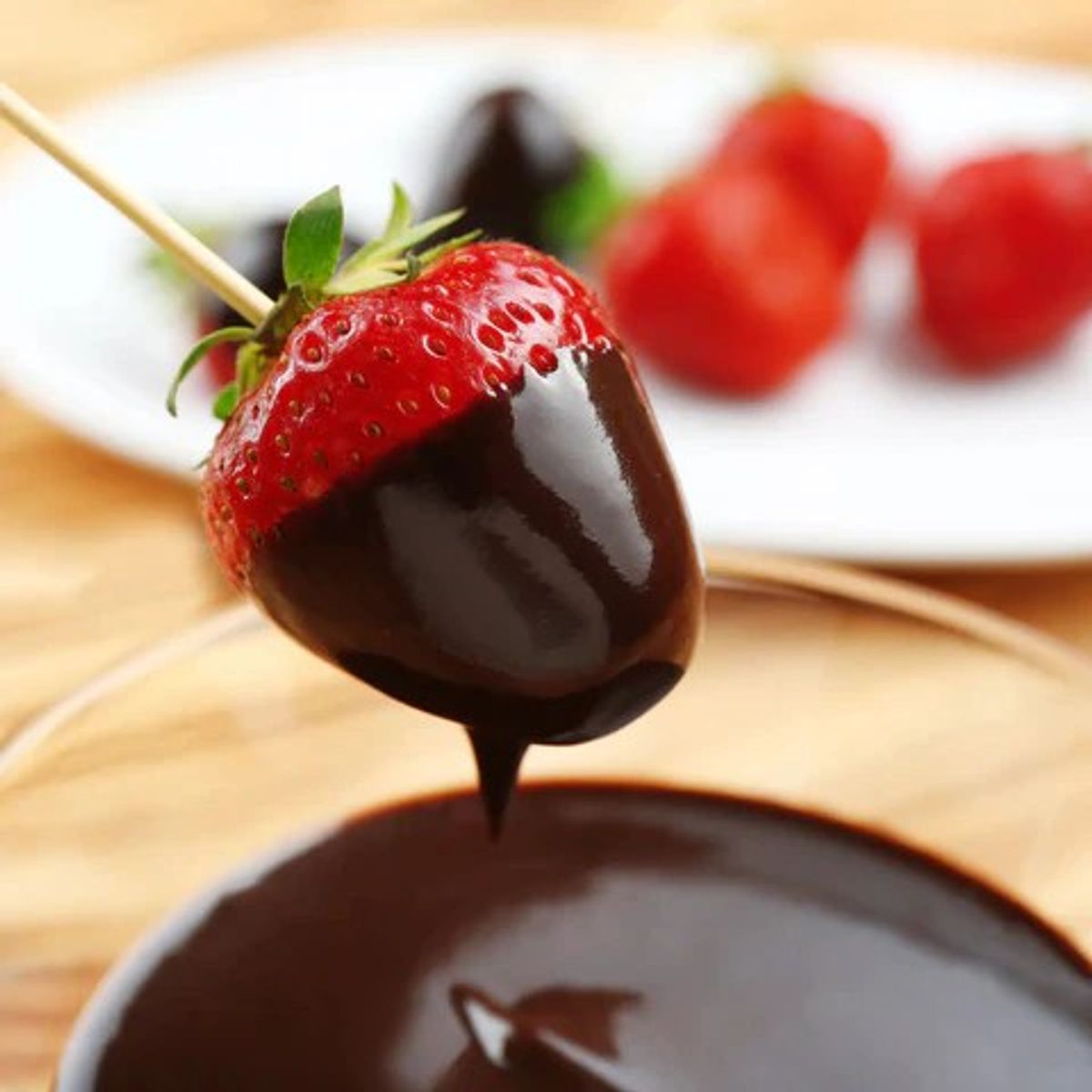 Chocolate-dipped strawberry on skewer with melted chocolate bowl and fresh berries