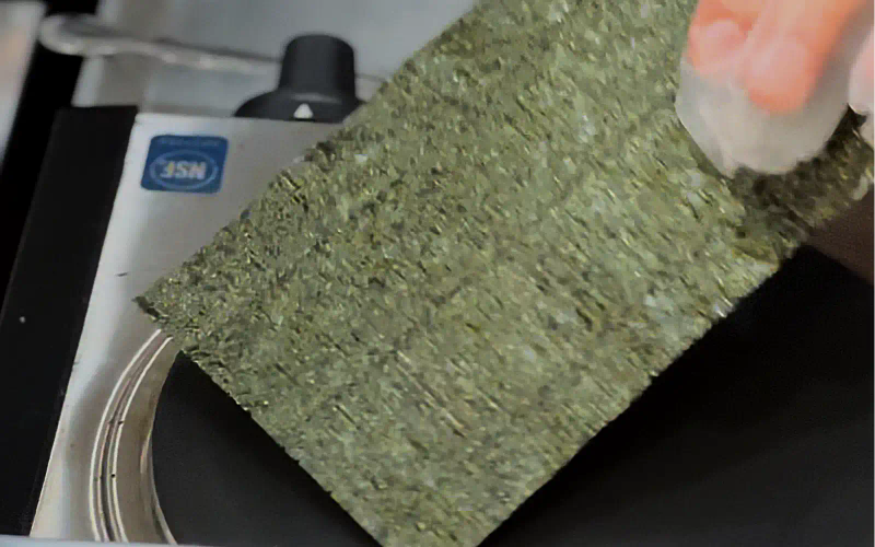 Nori seaweed sheet being held up next to measuring device for quality inspection