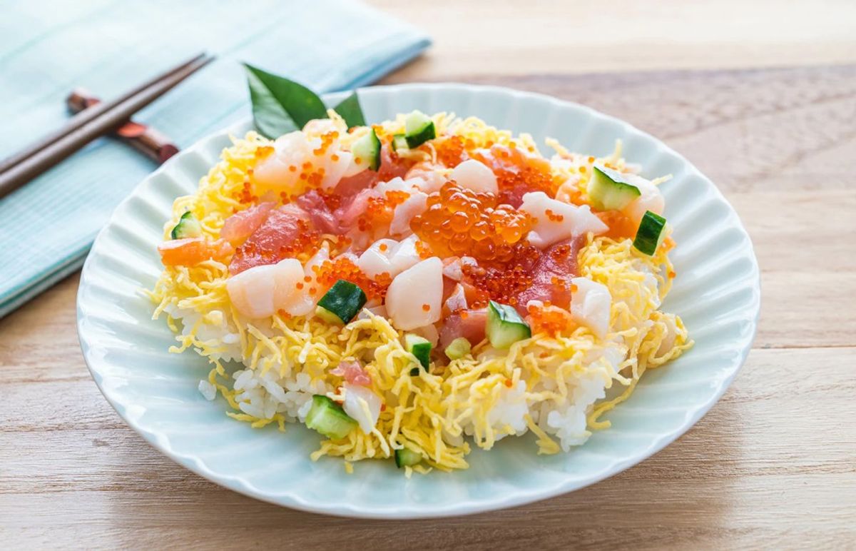 Chirashi sushi bowl with salmon roe, scallops, and crispy noodle base on white plate