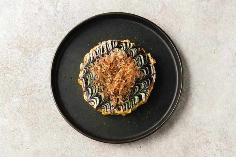 Decorative pastry with piped cream border and crumbled topping on black plate