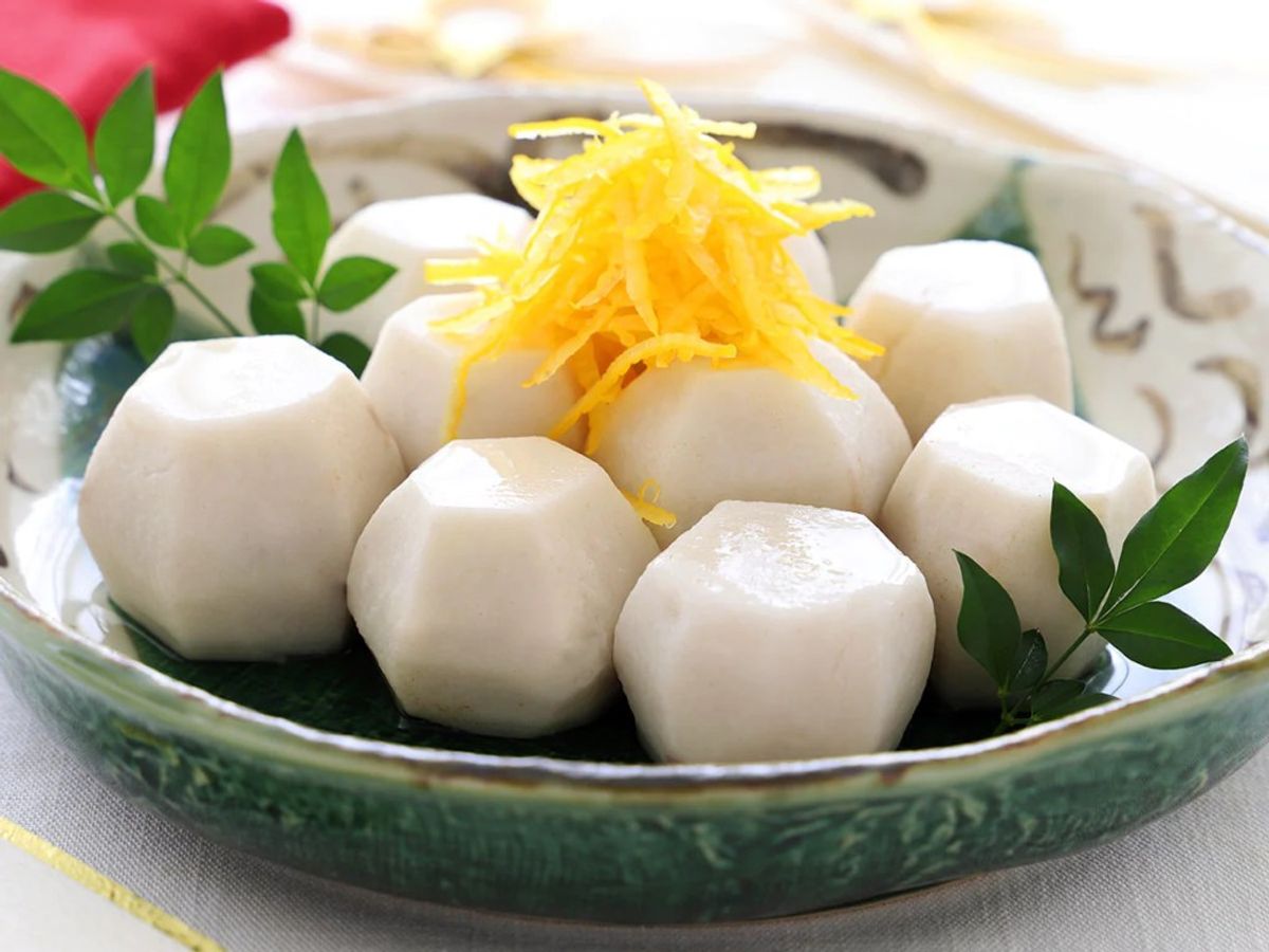 White mozzarella balls with shredded lemon zest, green leaves, in decorative ceramic bowl
