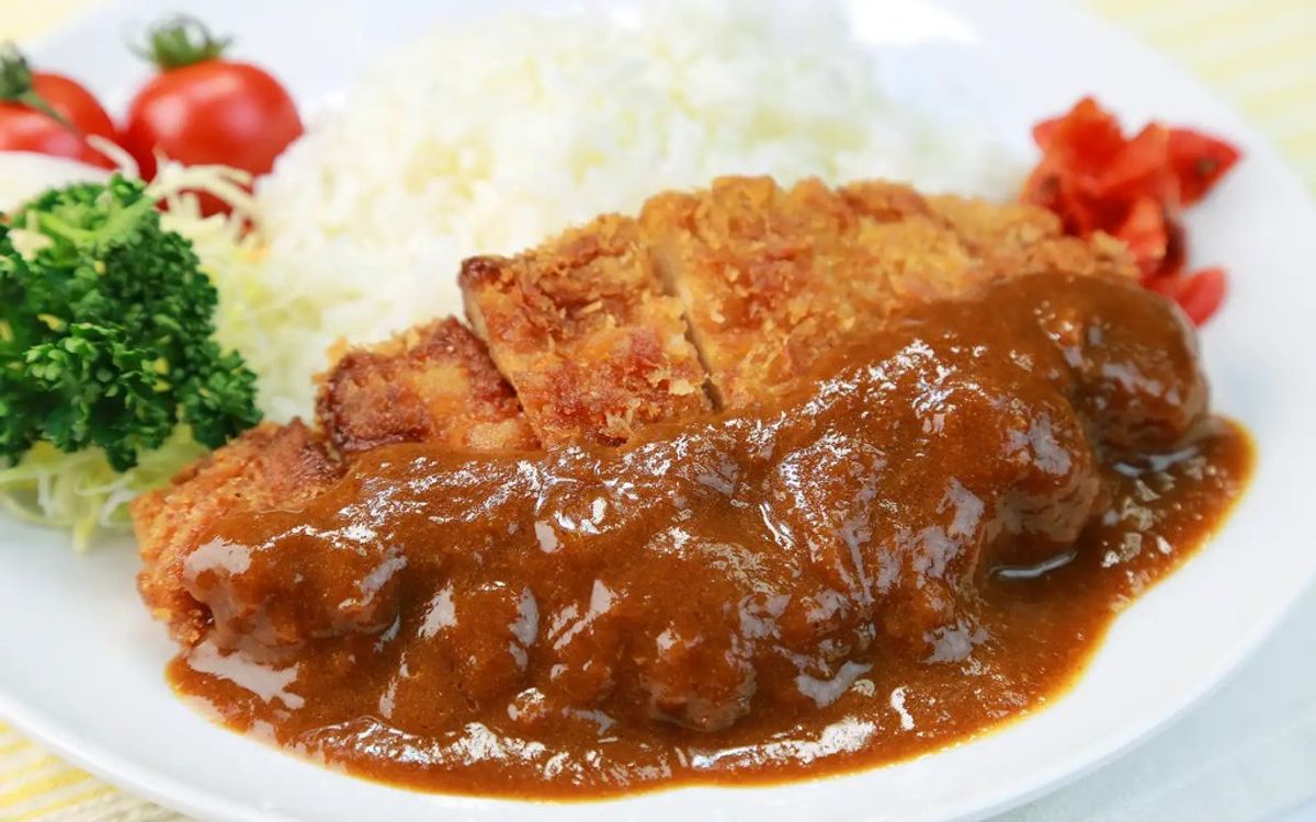 Breaded meat cutlet with brown gravy sauce, garnished with parsley and tomatoes on white plate