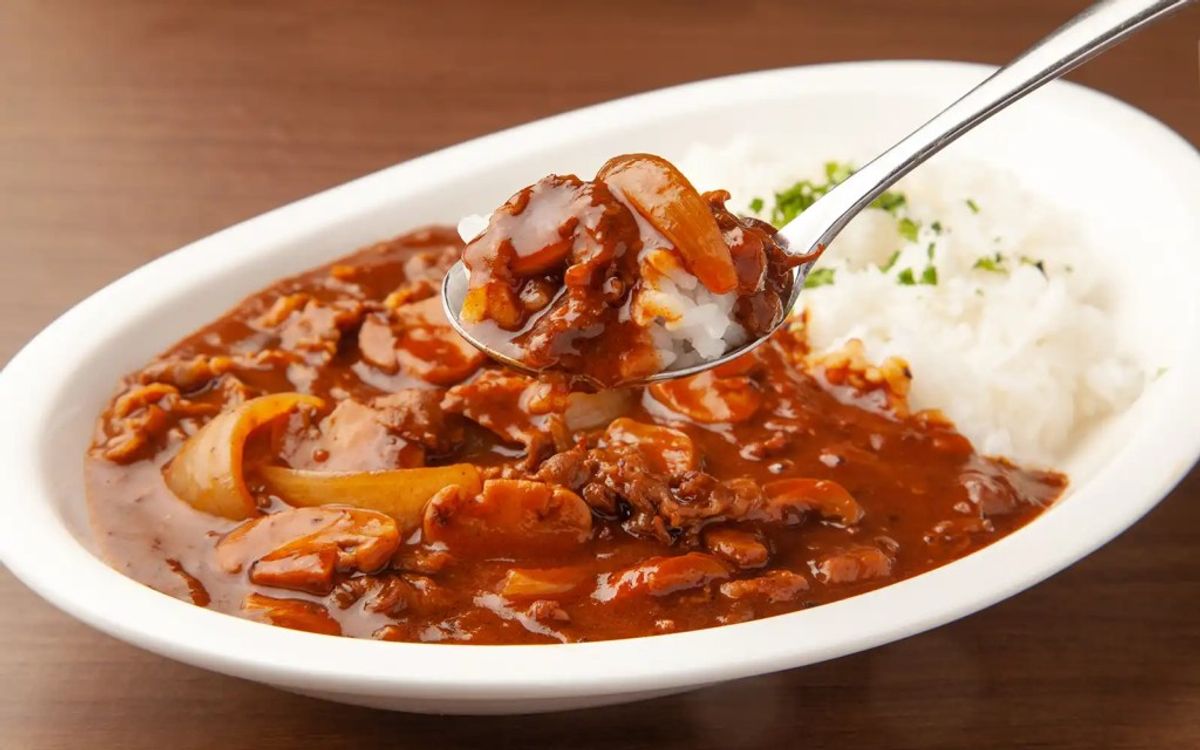 Beef goulash stew with onions served over mashed potatoes, spoon lifting portion
