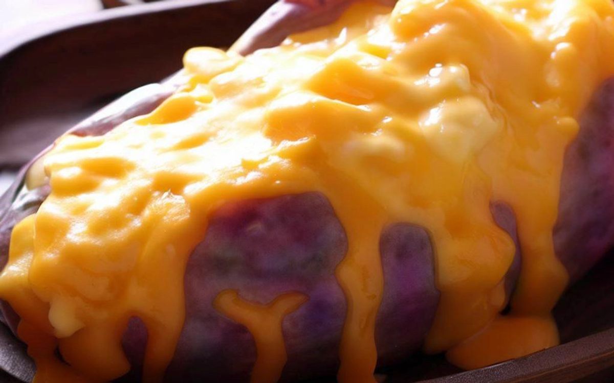 Baked potato topped with melted cheddar cheese on dark plate