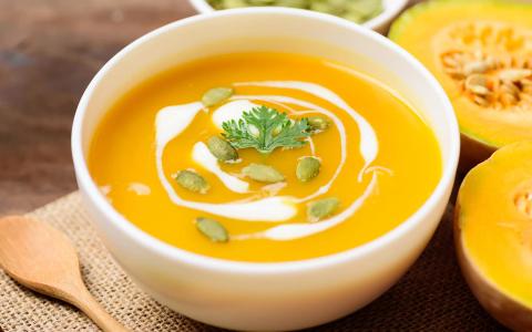 Creamy pumpkin soup with cream swirl, pumpkin seeds, and fresh herbs in white bowl