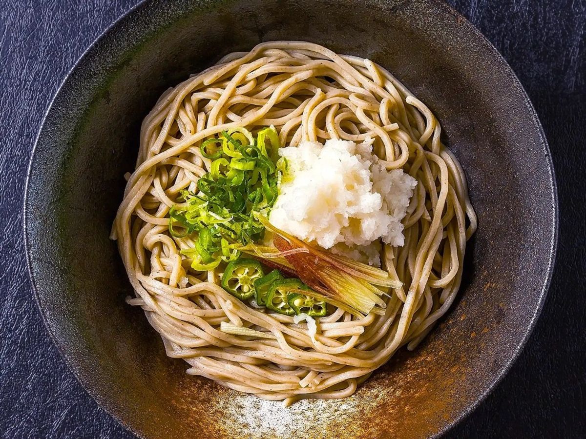Soba noodles in dark bowl topped with scallions and grated daikon radish
